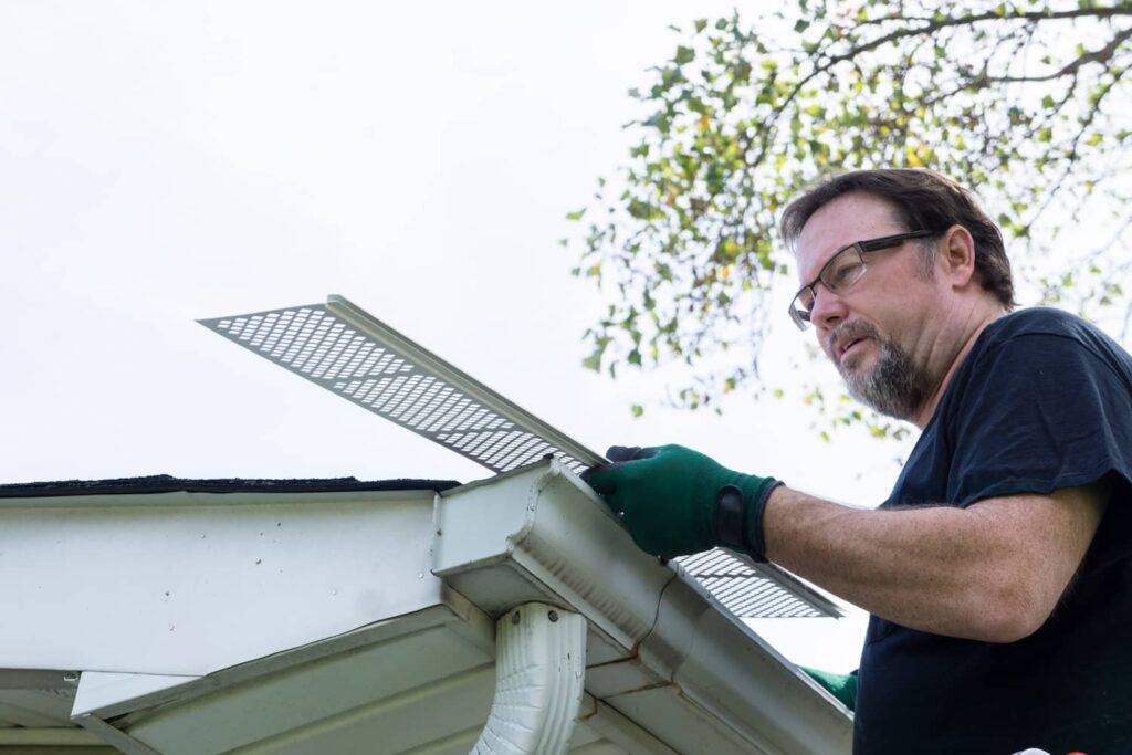 Person removing or replacing gutter guards for cleaning and maintenance